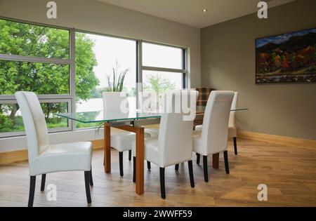 Tavolo con piano in vetro trasparente e sedie con schienale alto in pelle bianca nella sala da pranzo con pavimento in piastrelle di ceramica beige all'interno di una casa moderna in stile cubista, Quebec, Canada Foto Stock