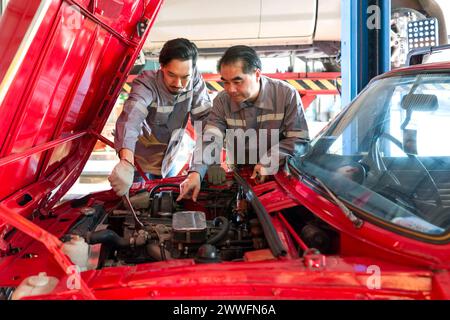 Due meccanici stanno lavorando su un'auto con il cofano aperto in un'officina automobilistica o in un garage. Sembrano concentrati e impegnati nella diagnosi o nella riparazione del ve Foto Stock