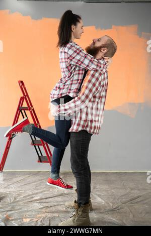 Giovane coppia di famiglie che sta facendo lavori di ristrutturazione a casa, dipingendo pareti e decorando la propria casa. Uomo e donna felici che si abbracciano in una nuova casa. Foto Stock