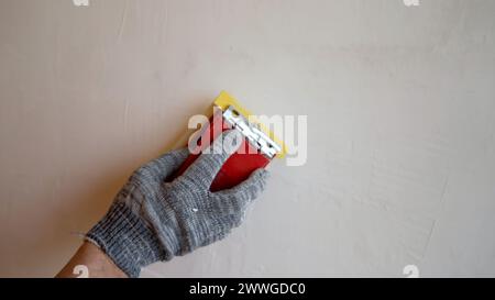 Rimuovere le superfici irregolari su una parete di stucco, levigare la superficie appena intonacata con carta vetrata. Pulire lo stucco con carta vetrata. Foto Stock