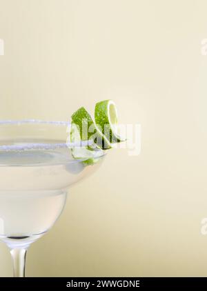 Primo piano di scorza di lime sul bordo di sale del bicchiere di margarita isolato su sfondo giallo pallido con spazio per il testo. Foto Stock