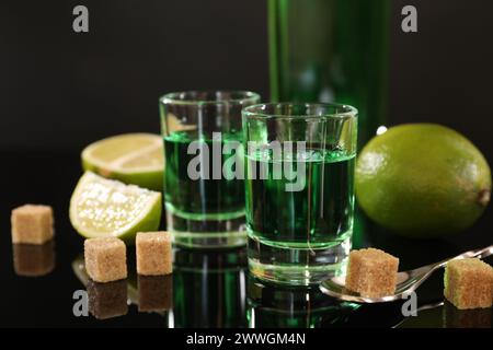 Absinthe in bicchieri da shot, zucchero di canna, lime e cucchiaio sul tavolo a specchio. Bevanda alcolica Foto Stock