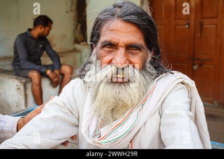 Un anziano uomo indiano del posto con la barba, in tipico abito di tutti i giorni, siede sul ciglio della strada in una città nel distretto di Umaria nel Madhya Pradesh, India Foto Stock