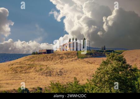 Architettura rurale in Toscana caratterizzata da una fattoria, cipressi e dolci colline sotto un cielo blu Foto Stock