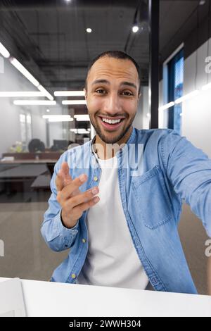 Un uomo sorride e indica qualcosa. Indossa una camicia blu e una camicia bianca. L'immagine ha un'atmosfera informale e amichevole Foto Stock