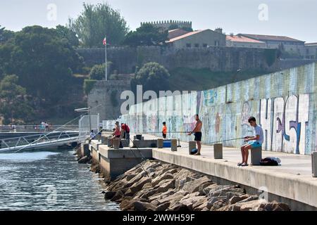 Baiona, Pontevedra, Spagna; 17 luglio 2022; i pescatori pescano con le loro canne dal frangiflutti di Baiona in una giornata molto calda e con il Parador sul retro Foto Stock