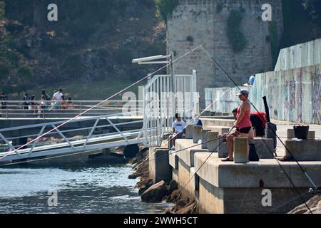 Baiona, Pontevedra, Spagna; 17 luglio 2022; i pescatori pescano con le loro canne dal frangiflutti di Baiona in una giornata molto calda e con il Parador sul retro Foto Stock