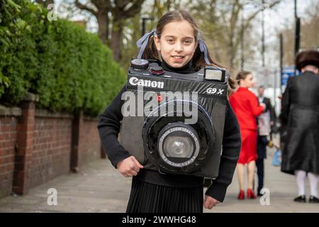 Londra, Regno Unito. 24 marzo 2024. Una ragazza a Stamford Hill, a nord di Londra, vestita con un costume da fotocamera Canon mentre celebrano il festival ebraico di Purim. Il festival prevede la lettura del Libro di Ester, che descrive la sconfitta di Haman, consigliere del re persiano, che complottò per massacrare il popolo ebraico 2.500 anni fa, ma l'evento fu impedito dal coraggio di Ester. Crediti: Stephen Chung / Alamy Live News Foto Stock