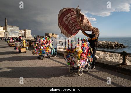 La tempesta si avvicina alla costa di Napoli, costringendo il venditore ambulante a coprire la sua stalla catturando la sua copertura nel vento Foto Stock