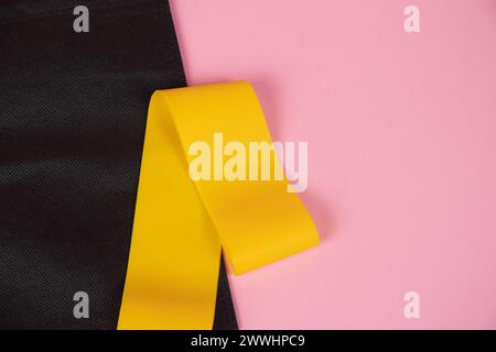 Fascia elastica gialla sportiva . Attrezzature sportive, sport a casa, articolo su sport, attrezzature per sport domestici. Elastico giallo su un backgroun rosa Foto Stock