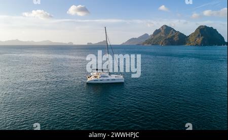 Vista aerea con droni dello yacht a vela ancorato nella baia con acque cristalline e turchesi al tramonto. Yacht a vela nella laguna tropicale. El Nido Foto Stock