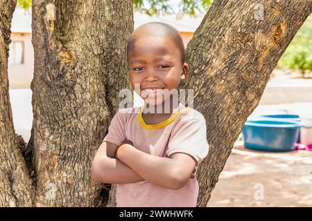 ragazzo africano del villaggio in piedi di fronte a un albero, nel cortile Foto Stock