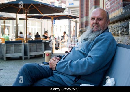 Uomo rilassante al Cafe Tilburg, Paesi Bassi. Uomo adulto senior che si rilassa su una panchina circondata dalla terrazza del caffè. MRYES Tilburg Stadscafe De Spaarbank Noord-Brabant Nederland Copyright: XGuidoxKoppesx Foto Stock