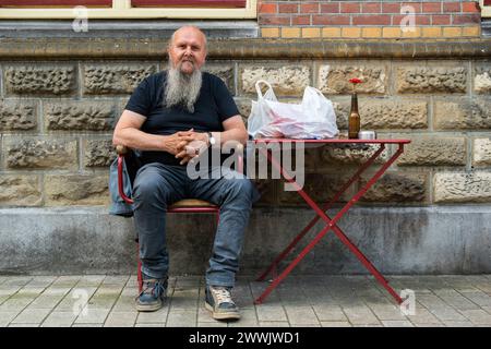 Uomo con la barba seduto a Tilburg, Paesi Bassi. Uomo adulto senior che si rilassa su una panchina circondata dalla terrazza del caffè. MRYES Tilburg Stadscafe De Spaarbank Noord-Brabant Nederland Copyright: XGuidoxKoppesx Foto Stock