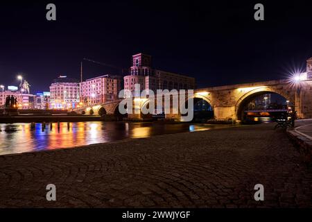 Edifici illuminati e luci vicino a un fiume di notte a Skopje, Macedonia settentrionale Foto Stock
