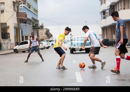 I giovani cubani calciano una palla di calcio giocando una partita in mezzo alla strada a l'Avana, Cuba. Foto Stock