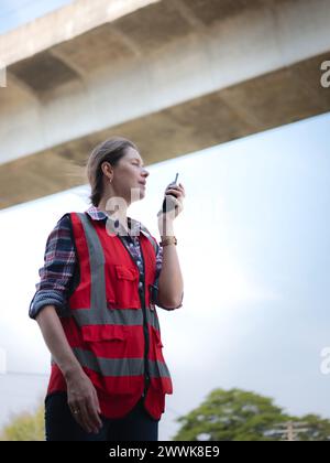 Una donna ingegnere ferroviario utilizza un walkie-talkie che parla con il reparto di manutenzione durante i lavori in cantiere del garage ferroviario. Foto Stock