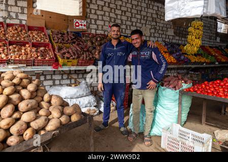 Due venditori di mercato che sorridono a braccetto tra prodotti freschi, Bahariya, Egitto Foto Stock