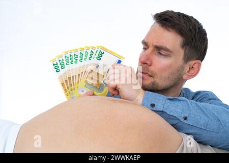 Descrizione: Il padre scettico conta mentalmente le spese future per il bambino e tira fuori le banconote della sua mano davanti al pregno della moglie Foto Stock