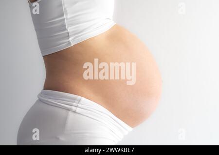 Descrizione: Parte centrale di una donna in piedi irriconoscibile con un batuffolo incinta molto rotondo. Vista laterale. Sfondo bianco. Colpo luminoso. Foto Stock