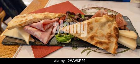 Tagliere di legno nero con formaggio, affettati, olive e focaccia a Roma, Italia. Primo piano, messa a fuoco selettiva. Foto Stock