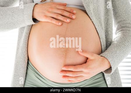 Descrizione: Vista frontale della sezione centrale di una donna irriconoscibile che tiene delicatamente la pancia negli ultimi mesi di gravidanza. Gravidanza primo trimestre - settimana Foto Stock