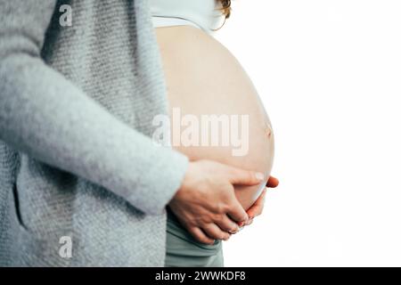 Descrizione: Vista laterale della sezione centrale di una donna irriconoscibile che tiene delicatamente la pancia negli ultimi mesi di gravidanza. Gravidanza primo trimestre - Wee Foto Stock