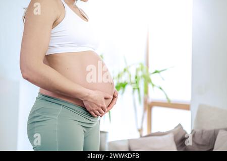 Descrizione: Vista laterale della sezione centrale di una donna irriconoscibile che tiene delicatamente la pancia negli ultimi mesi di gravidanza. Gravidanza primo trimestre - Wee Foto Stock