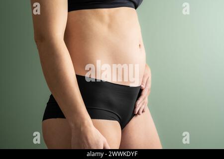 Descrizione: Vista in sezione intermedia di una donna irriconoscibile nei primi mesi di gravidanza che tiene la pancia con la mano sinistra. Prima la gravidanza Foto Stock