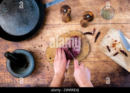 Descrizione: Donne che tagliano le mani bistecche di filetto di manzo crudo su un asse di legno con teglia d'acciaio, sale e pepe shakerand rosmarino e taglio freddo b Foto Stock