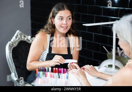 Donna esperta manicurista che filtra e forma le unghie di una cliente femminile durante la procedura di manicure nel salone di bellezza Foto Stock