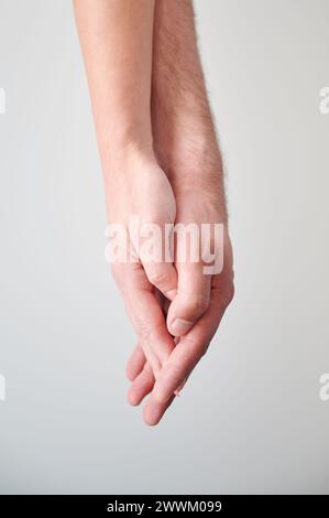 Vista ravvicinata delle mani della dolce coppia. Giovane uomo e donna che si tengono per mano su uno sfondo neutro e leggero. Concetto di amore, intimità, sostegno e fiducia. Foto Stock