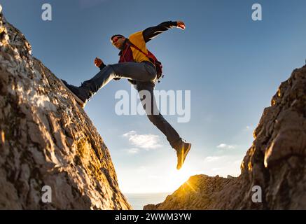 Giovane escursionista sportivo con zaino salta su una grande roccia contro il cielo del tramonto. Concetto di stile di vita attivo Foto Stock