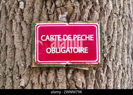 Un cartello è stato attaccato ad un tronco d'albero con scritto in francese "carte de pêche obligatoire", che significa in inglese "carta da pesca obbligatoria”. Foto Stock