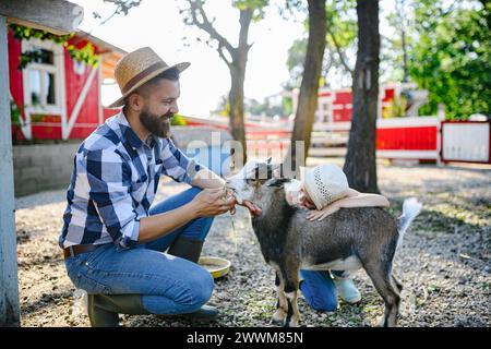 Ritratto del contadino che accarezza la capra nella sua fattoria. Uomo con cappello che lavora in un ranch di famiglia. Foto Stock