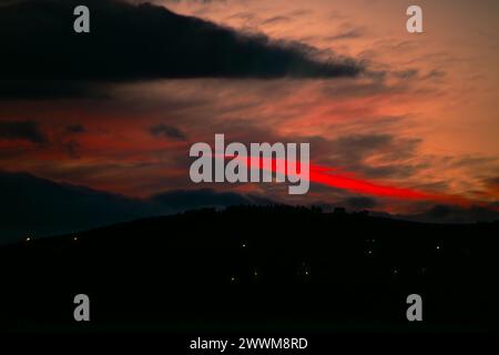 Nel tranquillo crepuscolo, un tramonto rosso inonda il cielo di sfumature ardenti, creando uno spettacolo suggestivo e celeste all'orizzonte. Foto Stock