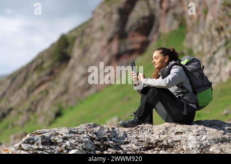 Escursionista che usa il telefono seduto su una roccia in montagna Foto Stock