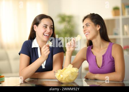 Due amici felici che parlano mangiando patatine a casa Foto Stock