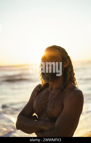 Ritratto dell'uomo felice con lunghi capelli ricci al tramonto sulla spiaggia. Foto Stock