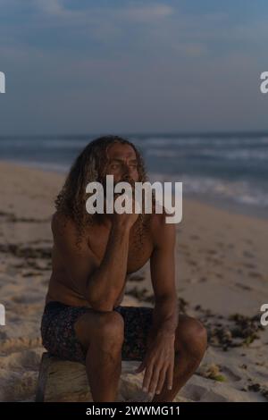 Ritratto dell'uomo felice con lunghi capelli ricci al tramonto sulla spiaggia. Foto Stock