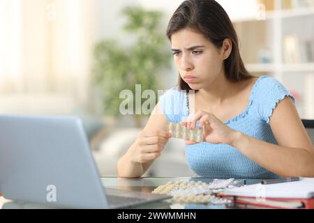 Studente stressato che prende pillole che studiano online con un portatile a casa Foto Stock