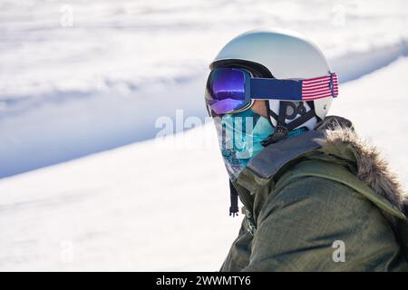 Primo piano di uno snowboarder contemplativo sulle piste, vestito con l'equipaggiamento invernale. Foto Stock