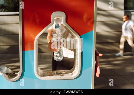 Donna che riempie la sua bottiglia d'acqua in città. Stazione di ricarica per bottiglie d'acqua pubbliche gratuita. Città sostenibile e verde. Acqua di rubinetto per ridurre il flacone di plastica Foto Stock