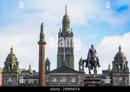 Dettagli dello skyline attraverso George Square, Glasgow, Scozia, Regno Unito verso le camere della città di Glasgow con la bandiera scozzese delle salme e le statue nella piazza. Foto Stock