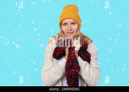 Ritratto ravvicinato di una donna anziana in un cappello a maglia, avvolto in una sciarpa contro il freddo su sfondo blu Foto Stock