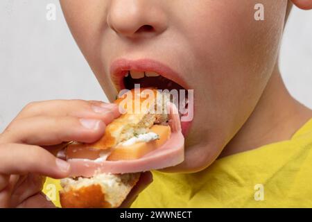 Le mani del bambino tengono un delizioso panino vicino alla bocca. Foto Stock