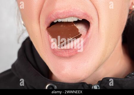 Una donna, il cui volto non è visibile, tiene un pezzo di cioccolato in bocca. Foto Stock