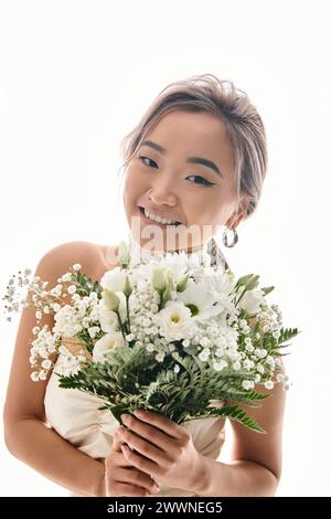 felice e seducente giovane donna asiatica sorridente alla macchina fotografica con bouquet di fiori bianchi su sfondo chiaro Foto Stock