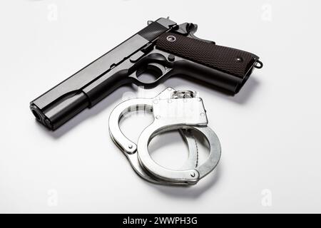 Pistola e manette su sfondo bianco Foto Stock