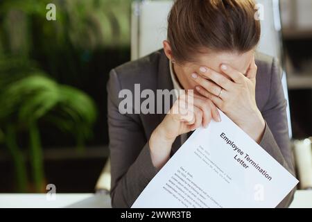 Nuovo lavoro. Primo piano su una donna moderna lavoratrice in un moderno ufficio verde in abito da lavoro grigio con lettera di licenziamento dei dipendenti. Foto Stock